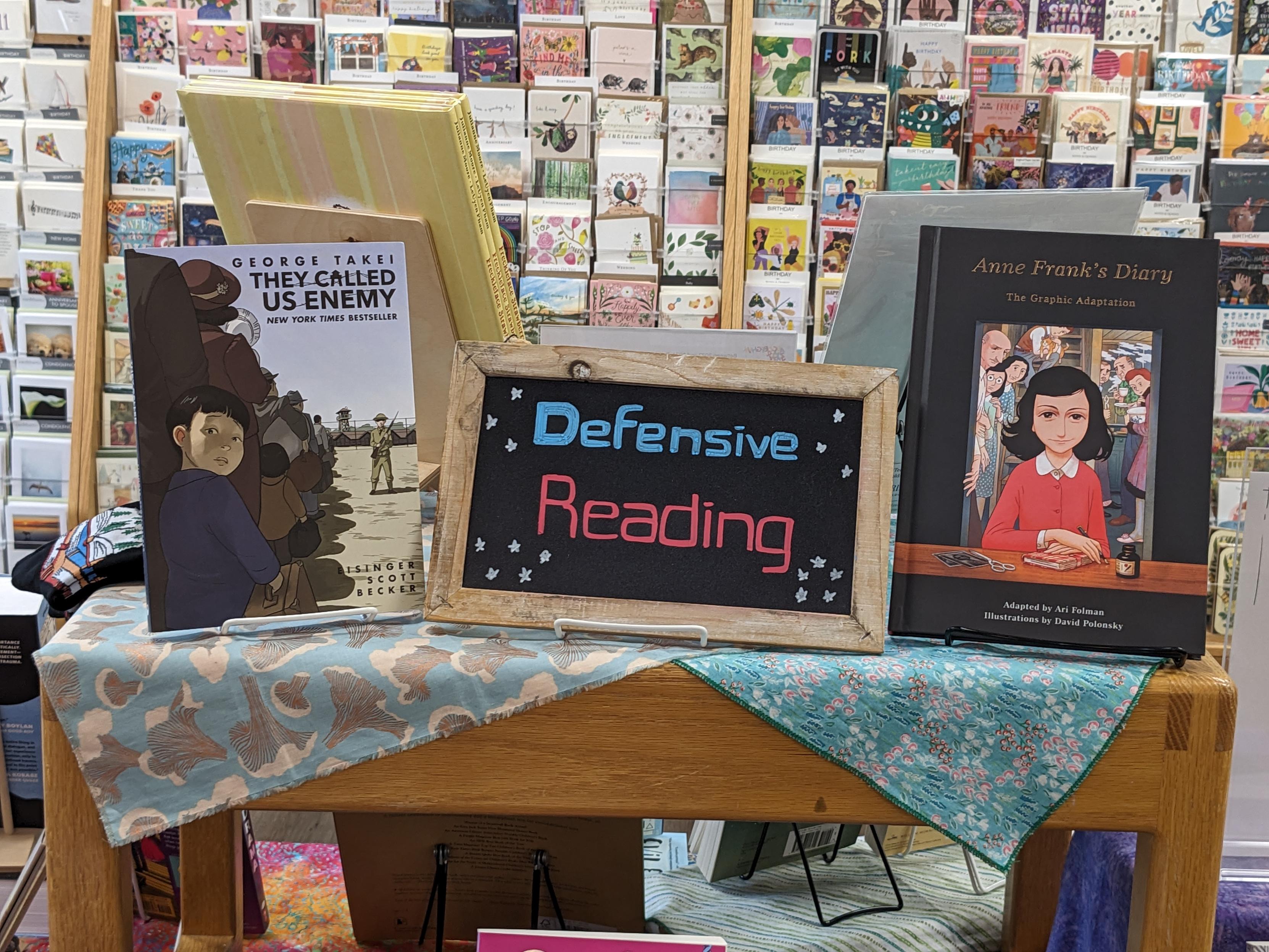 A display tableau in a book store titled "Defensive Reading" and featuring Anne Frank's Diary and George Takei's They Called Us Enemy, among others.