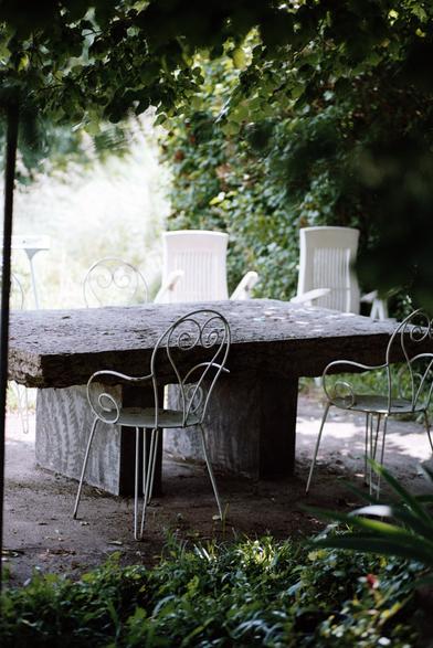 Une table en bois massif, entouré de chaises de jardin. La lumière et les bois, les invités ne sont pas là.