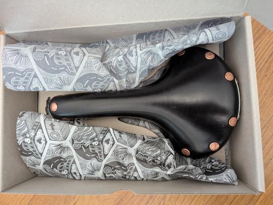 A Brooks leather bicycle seat in a box with some fancy tissue paper.