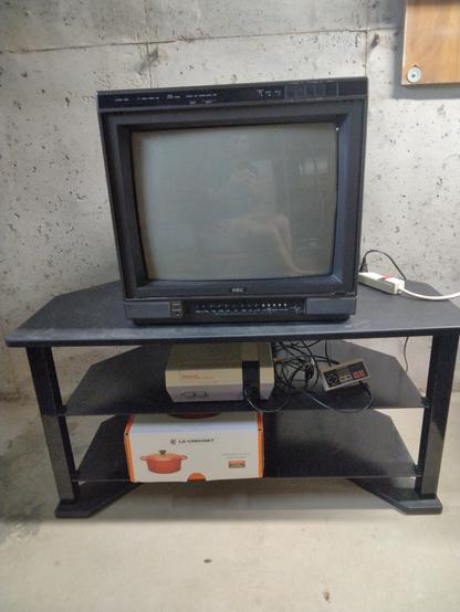 An NEC tube TV on a black TV stand with an NES, controller, and Le Creuset dutch oven box.