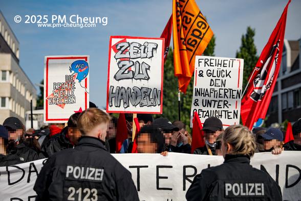 Zunächst wurde der Aufzug von der Polizei gestoppt, unter anderem weil Banner miteinander verbunden waren. Auf diesem Bild sind auch mehrere Schilder zu sehen, worauf u.a. "Zeit zu handeln", "Freiheit & Glück den Inhaftierten & Untergetauchten" und "Die rechte Welle brechen" zu lesen ist.