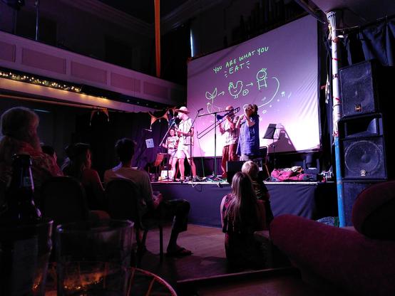 Formidable Vegetable on stage, part way through the song "You are what you eat".
Behind the band is a screen displaying pictures related to the song (fun fact: this is drawn live on stage by the DJ and Artist Brenna Quinlan)