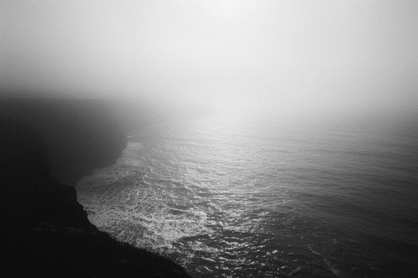 A black and white photo showing a view of cliffs looking out over the Irish Sea on a foggy day.