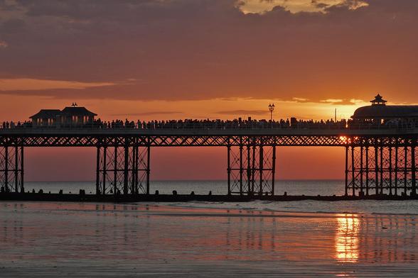 Crowded Cromer pier with the summer solstice sun setting behind it