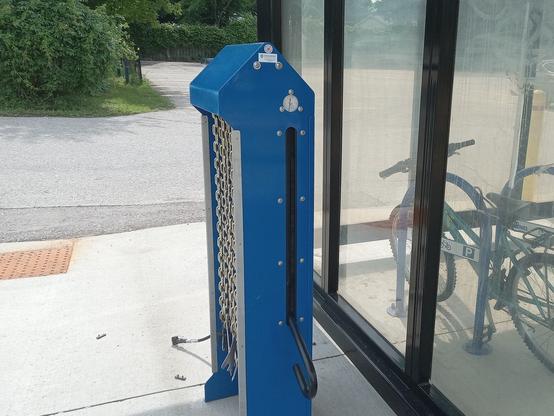 Side view of the repair station, showing the pump lever and the pressure gauge. To the right there's a bike parked in the bike shelter.
