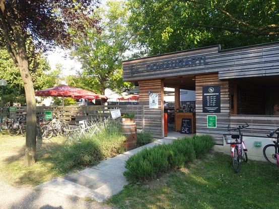 vor dem gebäude donaugartl sind fahrräder geparkt. auf der seite befinden sich sonnenschirme