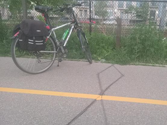 One of many inground bike sensor loops, looks like a double diamond, one in each bike lane, separared by a yellow line on the pavement. The post (with electronics? connections to Bike Central HQ?) can be seen in the grass at the back. Bob's bike is parked to the left, obstructing one lane. Tsk, tsk!