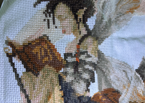 A fairy reads a book sewn via cross stitch.