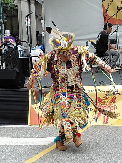 A grass dancer demonstrates footwork in front of a beating drum. Indigenous People's Day 2025.