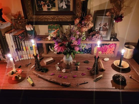 4 candles of varying color are lit on an altar and a fresh bouquet of flowers and herbs are in the middle.