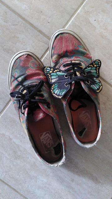 Chaussures vans rouges bleues et jaunes avec des lacets noirs. Sur les lacets de la chaussure de droite, il y a des ailes de papillons noires, bleues et jaunes
