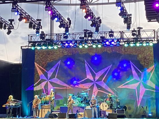 Ringo Starr and His All Starr Band performing in front of a 1960s psychedelic backdrop. The stars denote that they’re playing a country song.