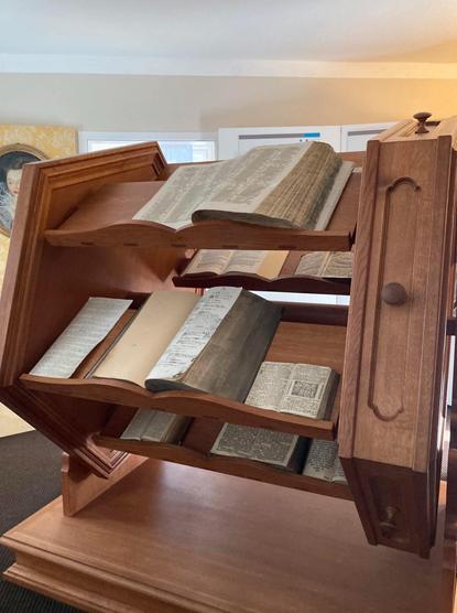 A wooden bookshelf displaying several open books of varying sizes. The structure is designed with curved shelves and has a rustic appearance, showcasing a mix of old and new texts. A soft background suggests an indoor setting.

Ein hölzernes Bücherregal mit mehreren offenen Büchern unterschiedlicher Größe. Die Struktur ist mit gebogenen Regalen gestaltet und hat ein rustikales Aussehen, das eine Mischung aus alten und neuen Texten zeigt. Ein weicher Hintergrund deutet auf eine Innenumgebung hin.