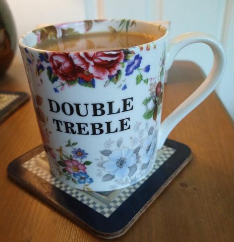 Floral pattern mug of tea on a bedside cabinet, with the words Double Treble in the middle