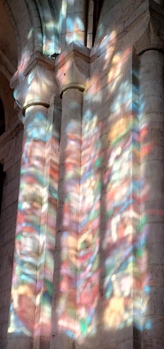 The light through a stained glass window falls onto a sandstone pillar
