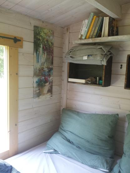 Der Schlafbereich im Tiny Haus mit Blick ins Grüne. Oben sind Bücher, wie zB "Baubiologisch Sanieren" oder "Das Parfüm". Am heißen Mittag will man aber lieber draußen am Fluss sein
