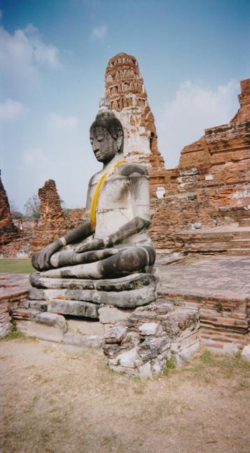Statue en pierre grise avec un tissu jaune sur l'épaule, dans la position du lotus, à Ayutthaya en Thaïlande.