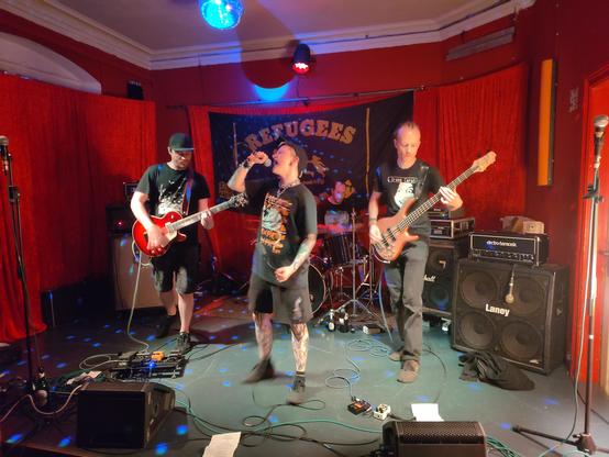 Punk Hardcore Band Profilachse from Berlin performing live on stage at the Tikozigalpa. There is a huge backdrop on stage that reads "refugees welcome".
