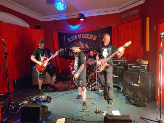 Punk Hardcore Band Profilachse from Berlin performing live on stage at the Tikozigalpa. There is a huge backdrop on stage that reads "refugees welcome".