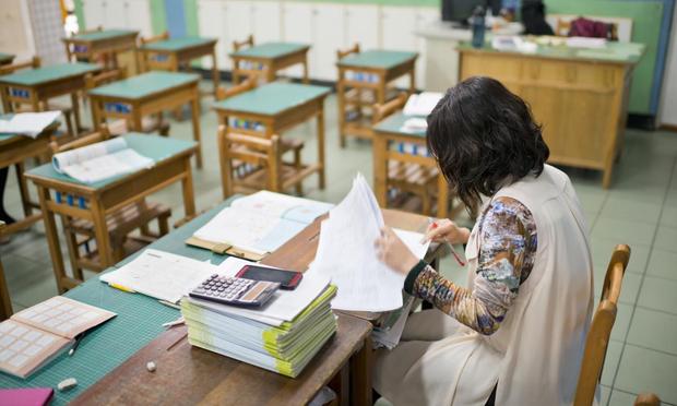 Female teacher is marking exam papers in classroom (LawrenLu; Leren Lu (Getty))