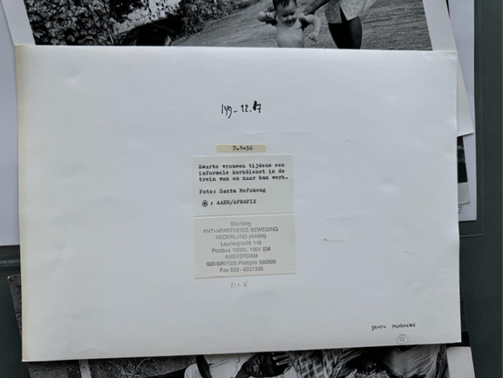 Verso of a photograph, with several archival references and a description: "Zwarte vrouwen tijdesn een informele kerkdienst in de trein naar hun werk. Foto: Santu Mofokeng"