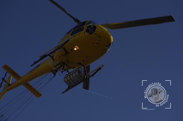 detalle de los bajos de un helicóptero amarillo volando a baja altura equipado con medios de extinción de incendios