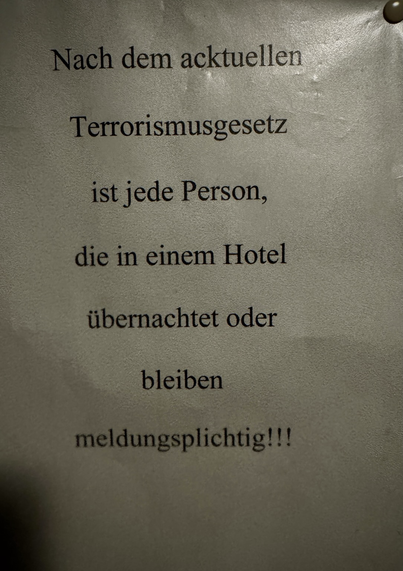 Auf einem an die Wand gehefteten Zettel stand der Spruch „Nach dem acktuellen Terrorismusgesetz ist jede Person, die in einem Hotel übernachtet oder bleiben meldungsplichtig!!!“