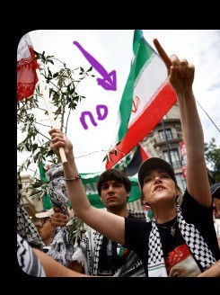 A protester in a black t shirt and cap wearing a keffiah and waving the the Islamic republic flag (green, white, red) which has the word allah in red in the middle.