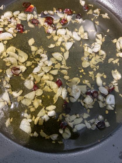 The bottom of a frying pan filled with olive oil, garlic slices and dried chili bits
