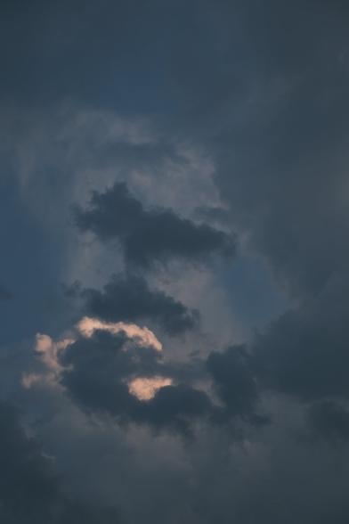 A cloud is illuminated by the sun, partially hidden by dark clouds in the foreground. The blue sky can almost be seen through the gaps, suggesting the end of the storm.