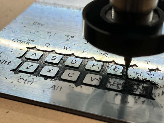 [ImageSource: Nicholas LaBonte]

The keys are on a single plate of little tabs, one for each key, that sits between the front panel and press on the tact switches inside.

The keyboard is especially interesting. On the inside it’s a custom PCB with tactile switches and a ATmega32U4 running QMK firmware [a popular choice for DIY keyboards] and presents to the host as a regular USB HID device.

How did he make those slick-looking keys? 

It’s actually a single plate that sits between the front panel and the switches themselves. [Nicholas] used a sheet of polymer with a faux-aluminum look to it and machined it down, leaving metal-looking keys with engraved symbols as tabs in a single panel. It looks really good, although [Nicholas] already has some ideas about improving it.