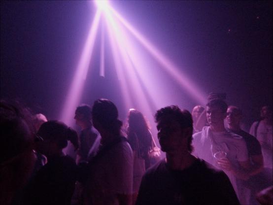 Another photo of a concert crowd. Sillhouettes of people are set against bright purple beams of light connecting at the top of the frame.