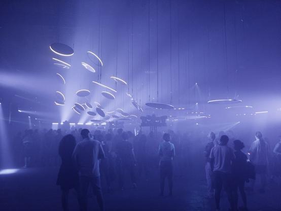 A large array of mirror disks floating in the big concert hall, their rims shining bright. The crowd is lost in the dense haze.