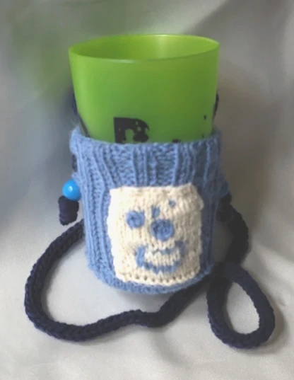 Le porte-gobelet "Mageia" bleu avec un rectangle crème sur lequel figure le motif du chaudron de Mageia. La lanière est bleu marine. Le gobelet vert provient des rencontres mondiales du logiciel libre de Beauvais en 2015.