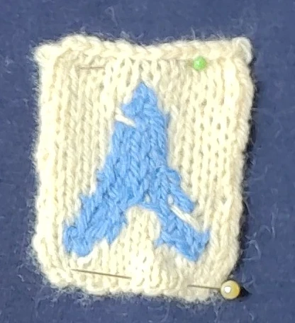 Le a du logo d'archlinux tricoté en bleu sur un fond crème.