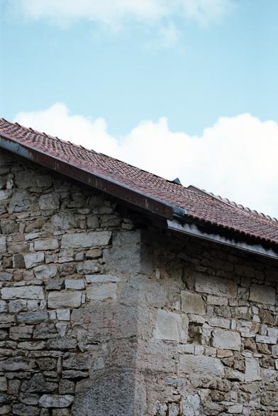 Maison en pierre, toit en tuiles rouges. Ciel bleu, nuages et perspective. Tout est raccord.