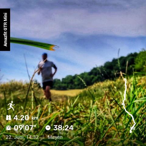 Eine Person joggt auf einem sonnigen Feldweg, flankiert von hohem Gras. Im Hintergrund stehen Bäume unter einem klaren, blauen Himmel. Am linken Bildrand ist ein schwarzer Balken mit der Aufschrift ‚Amazfit GTR Mini‘ eingeblendet. Unten links werden Laufdaten angezeigt: 4,20 km Strecke, Pace von 9:07 min/km, Laufzeit 38:24 Minuten, Datum 22. Juni, Uhrzeit 14:32, Ort Mayen. Rechts unten ist eine Karte mit der gelaufenen Strecke zu sehen.