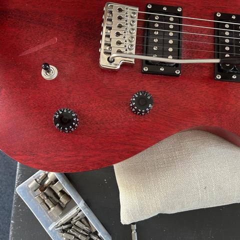 Closeup of the front of the guitar, showing the too small distance mentioned - it's lying on a grey pillow and there are some screw bits in a small bin next to it