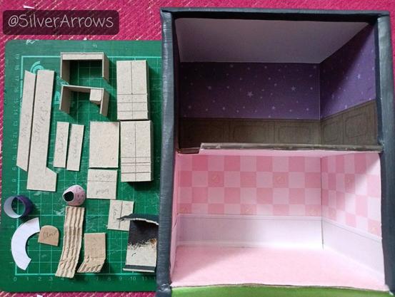Work in progress of the new dollshouse project. On the right is the frame for the house. The ground floor is pink and white themed. The first floor is black and purple. On the left are some unfinished bits of furniture made from greyboard.