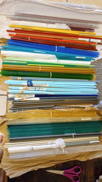 Photo of a large number of glass rods and canes, bundled up and arranged by colors, used in hot glass work (lampwork or torch work).