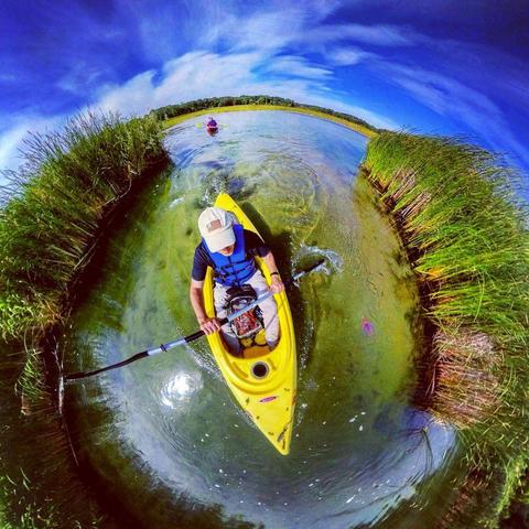One of a series of photographs in which two people are pictured hiking, biking, and kayaking throughout a beautiful and verdant state park in central Minnesota under cloudy blue late-summer skies.