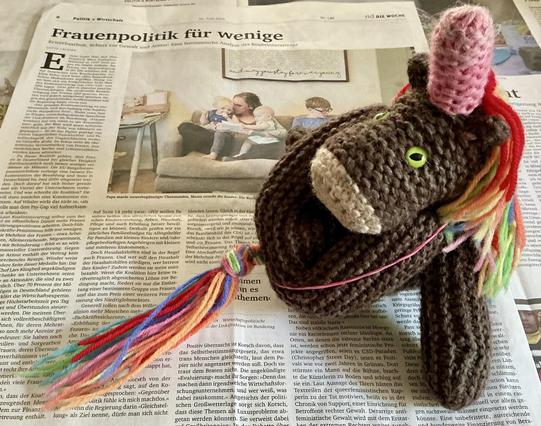 Max, das bunte Strickhorn, in einer spannenden Yoga-Position: seine Hinterpfoten werden mit einem Gummiband fast an die Ohren gehalten.