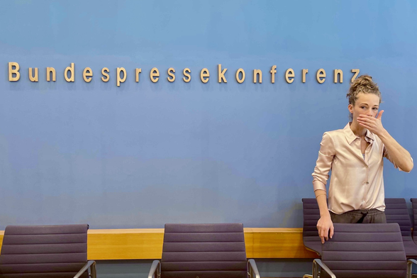 Helena Steinhaus vor der blauen Wand der Bundespressekonferenz, hält sich die linke Hand vor den Mund