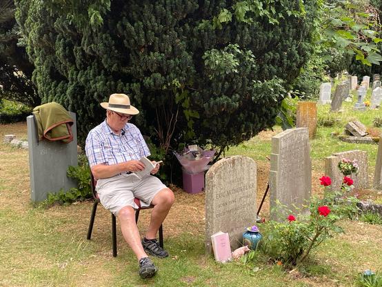 George Orwell‘s son Richard Blair sits next to his father’s grave, reading from one of Orwell‘s texts (The Clergyman‘s Daughter)