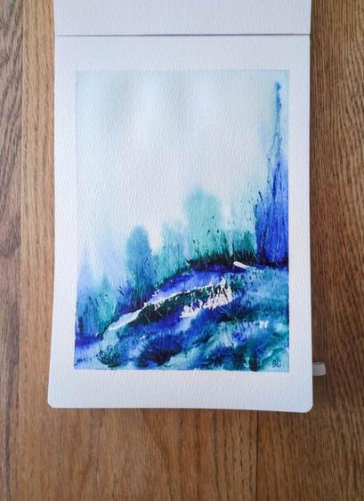 This is An Atmospheric Watercolor Landscape Painting in portrait orientation in an A5 sketchbook. Colors used are Daniel Smith Ultramarine Turquoise and Winsor and Newton French Ultramarine Blue. These colors are granulating and have explosive movement, which occurs at the curving horizon line. There are clear bursts of medium value blue and turquoise but also a mixture of the two. There colors are diluted to a light value in the atmosphere with grasses slicing through the medium value. At the horizon line there are dark values and more through out the landmass with some medium and light values and a few bits of unmarked white paper showing through. In the piece the colors are vibrant and create a sense of luminosity.