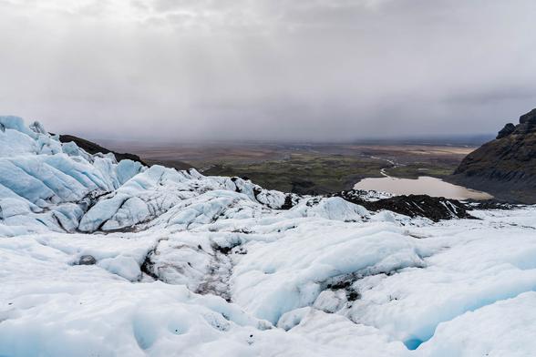 Wide-angle view of the icy crevasses and snowy ridges of Falljökull glacier, taken from the upper section of a guided glacier hike in Skaftafell Nature Reserve, Iceland. Rugged mountains rise in the distance under a soft, overcast sky.