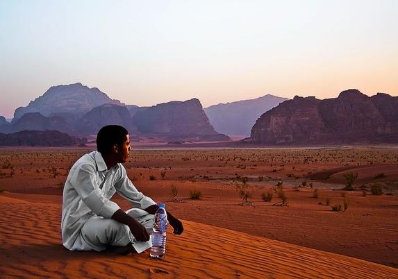 photo of a Jordanian Bedouin sitting on a large orange sand dune looking out over the famous and mind bending desert of Wadi Rum just after sunset while the air still glows with a lavender sheen, on a processing note - i was just learning photoshop and went a bit overboard with the sharpening smoothing sliders - lesson learned!