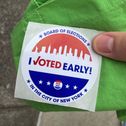 My shitty hand holds a red and blue “I Voted Early” sticker given in NYC for voting. The sticker depicts an NYC skyline with the Statue of Liberty and all the iconic skyscrapers.