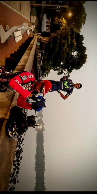 The photograph shot by an amateur, shows two passionate cyclists near a body of water, with a streetlight illuminating the scene. The person in the foreground is wearing a red motorcycle racing suit with "SONY MUSIC STUDIO" and "ANCOTOPROS" written on it, along with a red helmet and blue gloves, and is interacting with a Android phone taking a serene photograph of the other side. The second person, standing behind, is dressed in a dark blue cycling outfit with a green logo and a black cap, smiling and holding a phone. The background features a calm water surface reflecting the trees and sky, with a brick wall and steps leading down to the water. The sky is overcast, and the overall lighting suggests it is either early morning.

Ovis2-8B

🌱 Energy used: 0.855 Wh