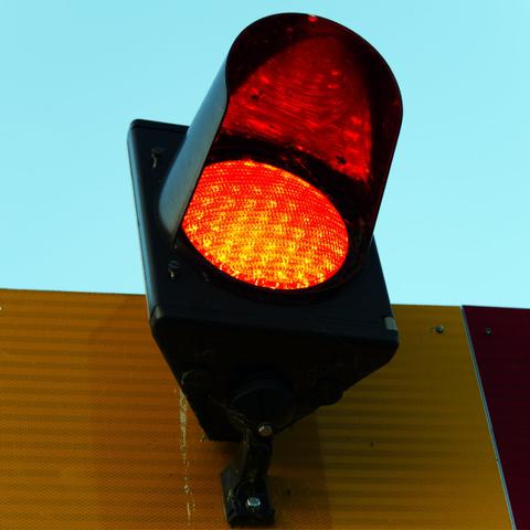 Close-up of an illuminated red maritime shore marker light (similar in appearance to a traffic light) against a clear blue sky.